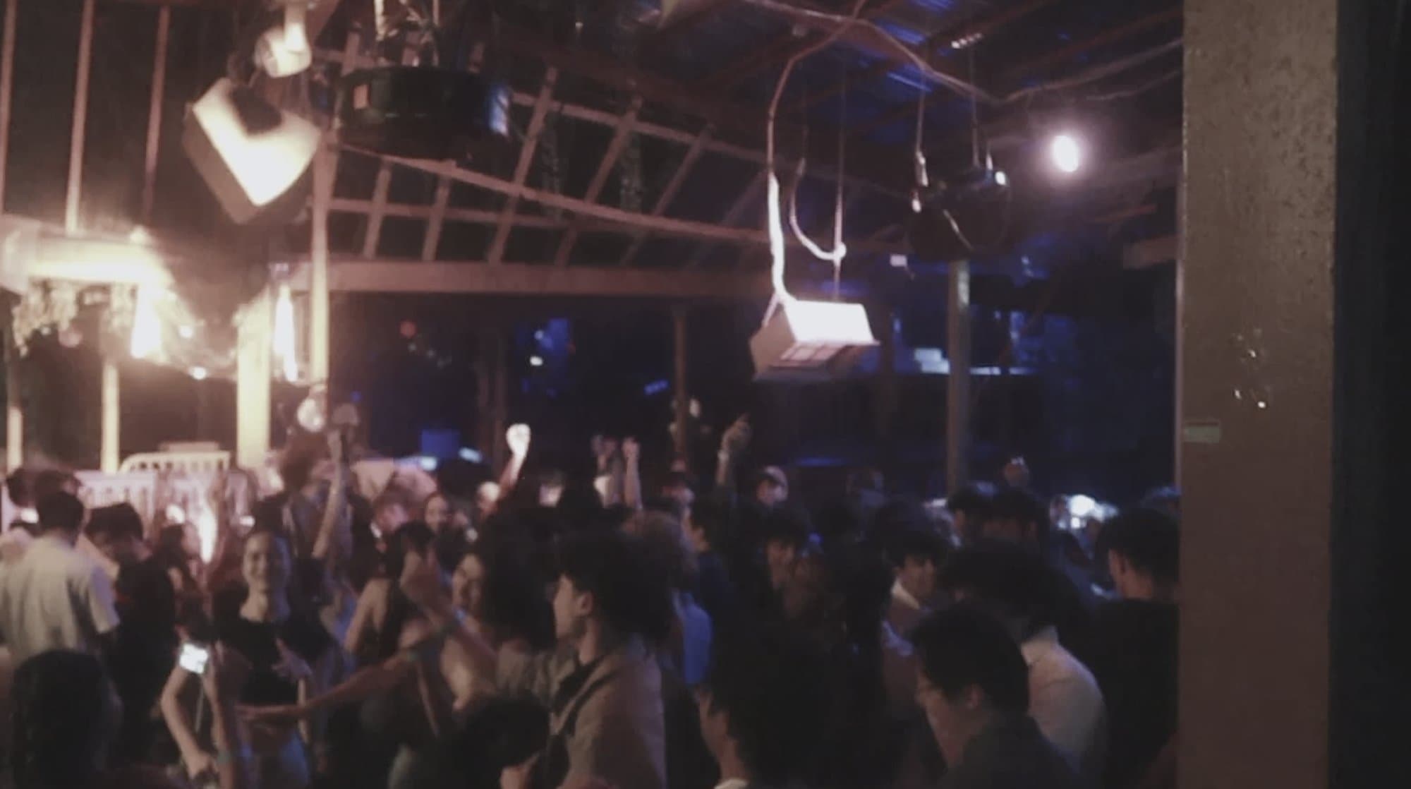 A crowded warehouse floor under rafters and stage light, late into a takeover